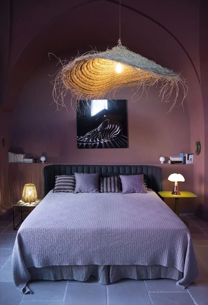 Doppelbett mit lila Tagesdecke unter einer großen Lampe aus Naturfasern.
