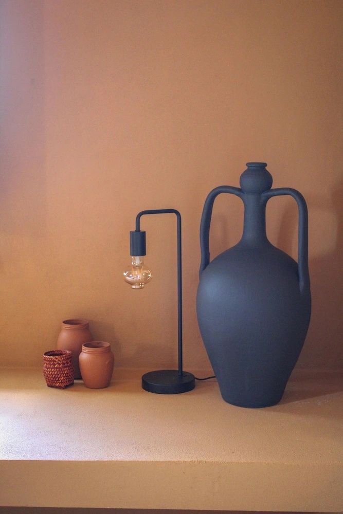 Große dunkle Tonvase neben einer modernen Metalllampe vor einer terracottafarbenen Wand.