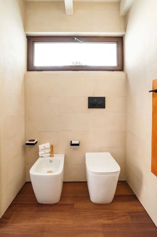 Helles Badezimmer mit weißer Toilette, Bidet und beigefarbenen Wandfliesen.