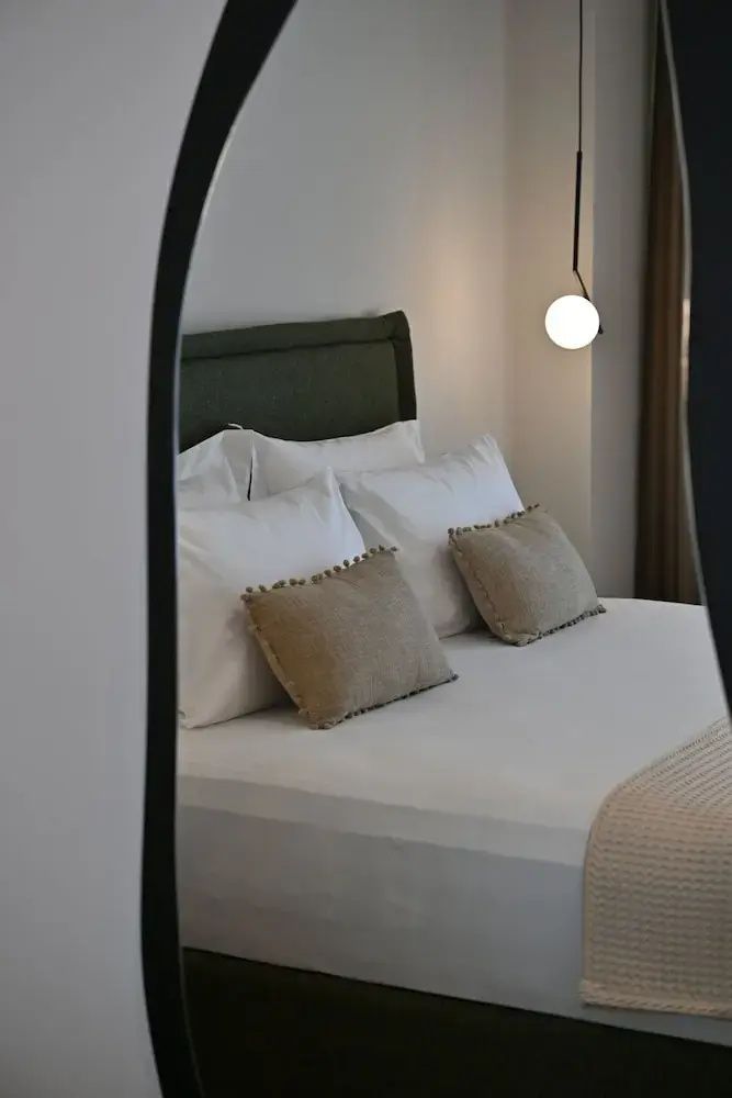 Doppelbett mit weißer Bettwäsche, dunkelgrünem Kopfteil und beigen Kissen im Spiegelrahmen.