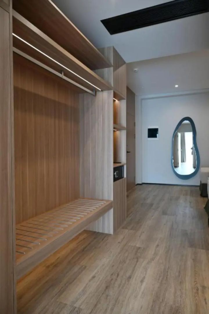 Offener Holzkleiderschrank mit Regalfächern und Safe in einem modern gestalteten Hotelzimmer.