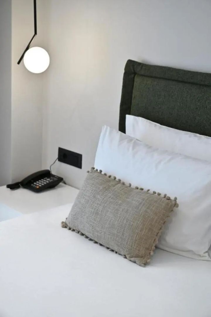 Doppelbett mit weißen Kissen, grauem Dekokissen und gepolstertem Kopfteil neben dem Nachttisch.