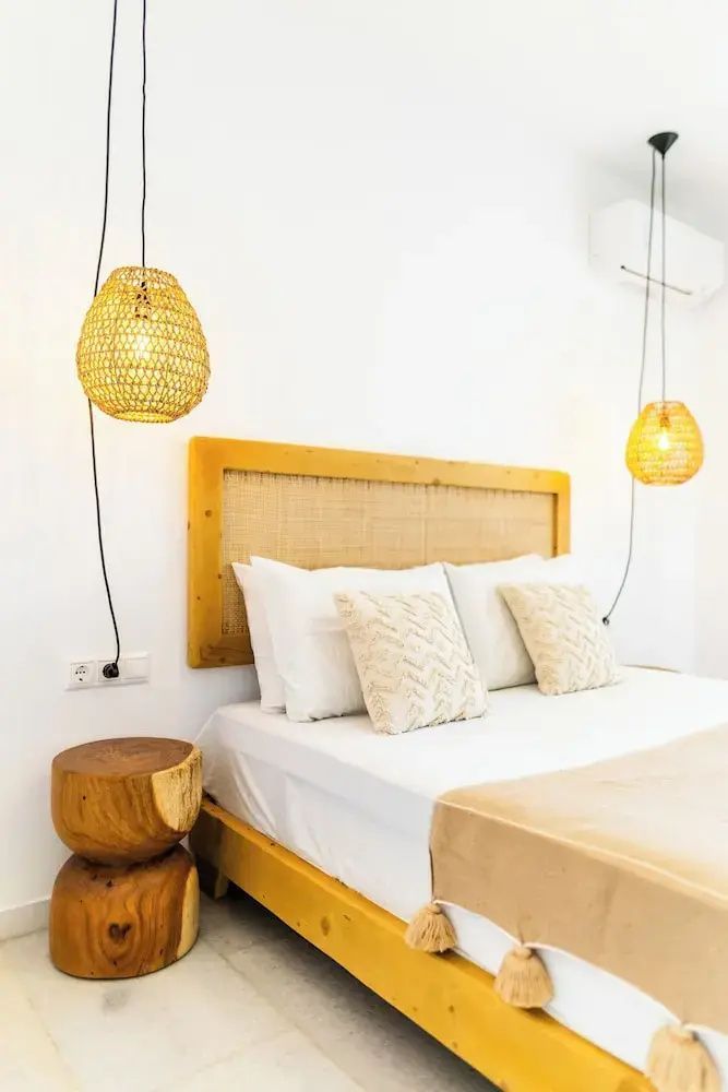 Doppelbett mit Holzkopfteil, zwei Kissen und hängenden Lampen aus Geflecht.