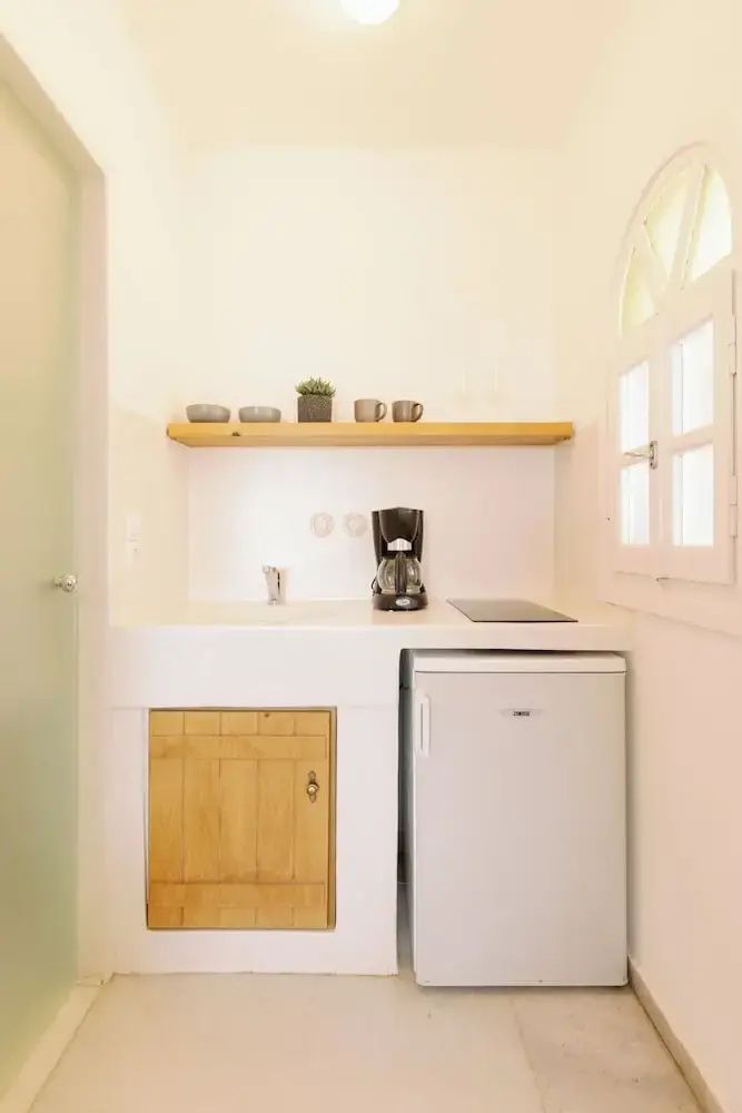 Kompakte Küchenzeile mit Kühlschrank, Kaffeemaschine, Kochfeld und Wandregal.