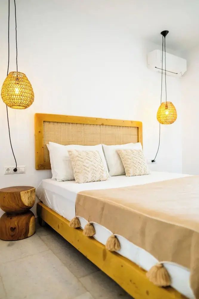 Doppelbett mit Kopfteil aus Holz, beigefarbener Tagesdecke und zwei Hängeleuchten aus Geflecht.