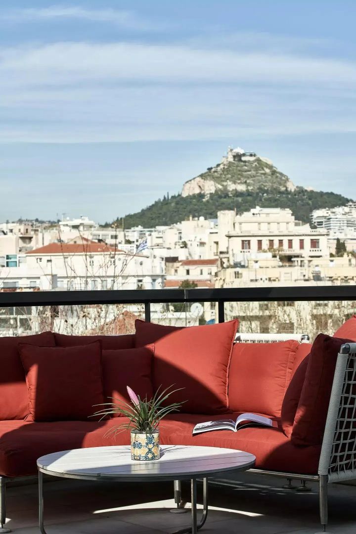 Dachterrasse mit roten Polstermöbeln und Blick auf die Stadt und einen Hügel.