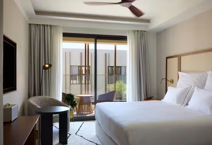Heller Hotelraum mit Doppelbett, Sitzbereich und Zugang zum Balkon.