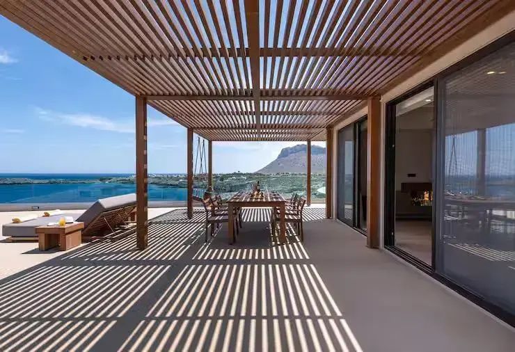 Terrasse mit hölzerner Pergola, Esstisch und Panoramaaussicht auf Meer und Berge.