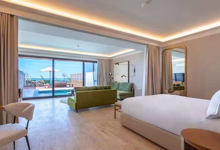 Geräumiges Hotelzimmer mit Doppelbett, grünem Sofa und Terrasse mit Meerblick.