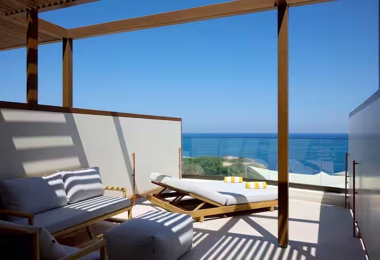Überdachte Terrasse mit Holzpergola, Sitzmöbeln, Sonnenliege und Meerblick.