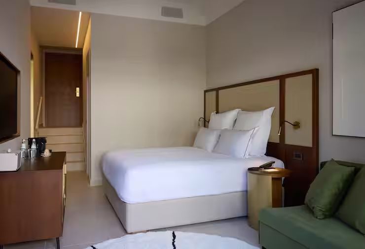 Modernes Hotelzimmer mit weiß bezogenem Doppelbett und Holz-Kopfteil.