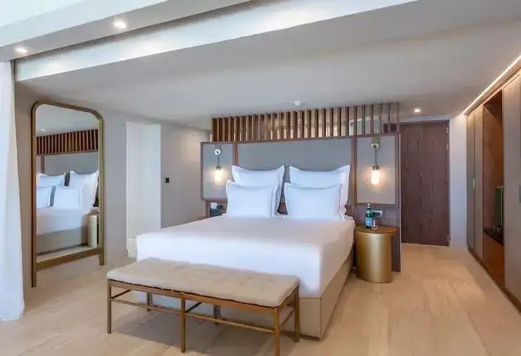 Großes Doppelbett mit weißer Bettwäsche und Holz-Kopfteil im hellen Hotelzimmer.