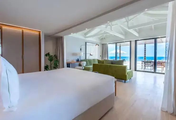 Hell eingerichtete Suite mit Bett, grüne Couch und Blick auf den Strand und das Meer.