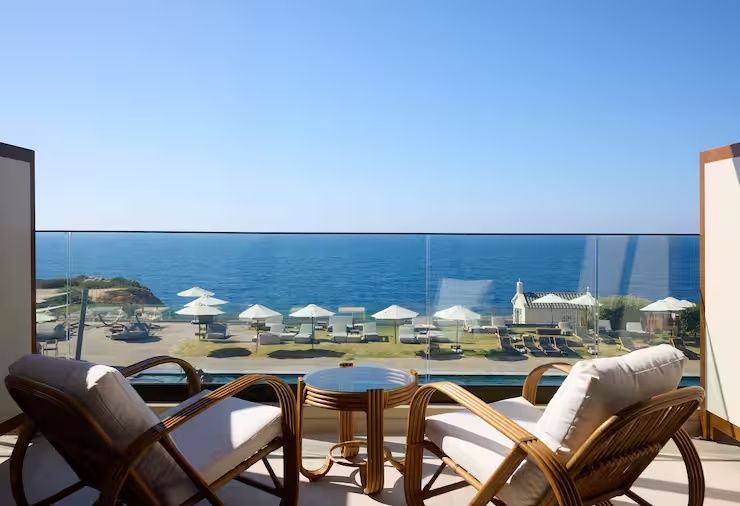 Balkon mit zwei Rattanstühlen und Glastisch mit freier Sicht auf das Meer.
