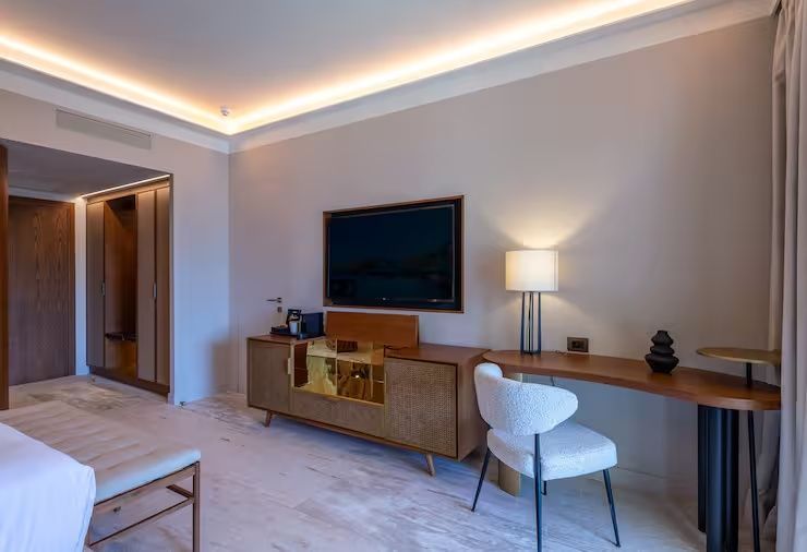 Schreibtisch mit weißem Stuhl, Fernseher an der Wand und Sideboard aus Holz im Zimmer.