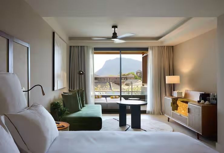 Helles Hotelzimmer mit Doppelbett, grünem Sofa und Balkonaussicht auf die umliegende Berglandschaft.