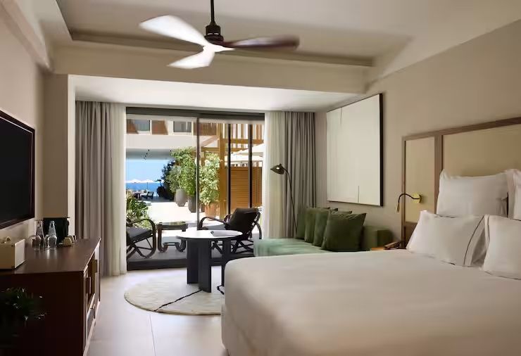 Geräumiges Hotelzimmer mit Deckenventilator, Sofa und Blick nach draußen.