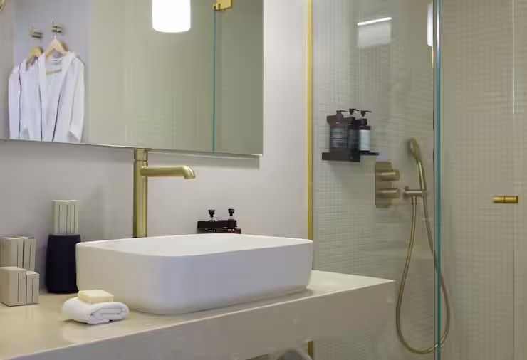 Modernes Badezimmer mit weißem Aufsatzwaschbecken, goldener Armatur und einer Glasdusche.