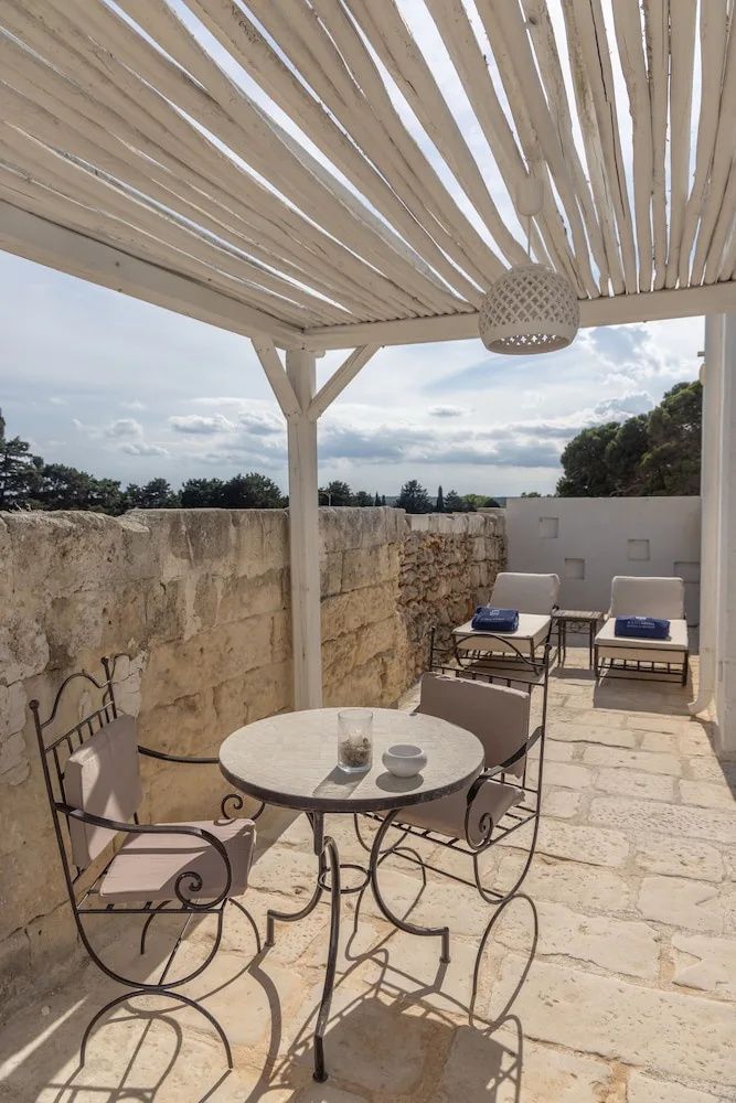 Terrasse mit Steinmauer, hölzernem Sonnendach, runder Sitzgruppe und zwei Sonnenliegen.