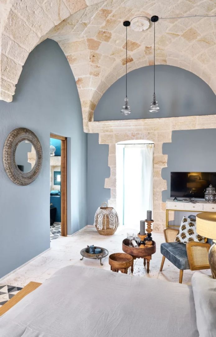 Wohnbereich mit blauen Wänden, historischen Steinbögen, Sessel und Fernseher.