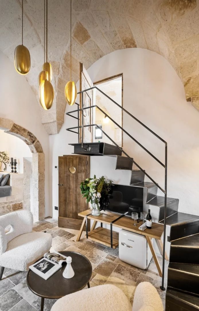 Wohnbereich mit historischem Kreuzgewölbe, moderner Stahltreppe und Designleuchten.