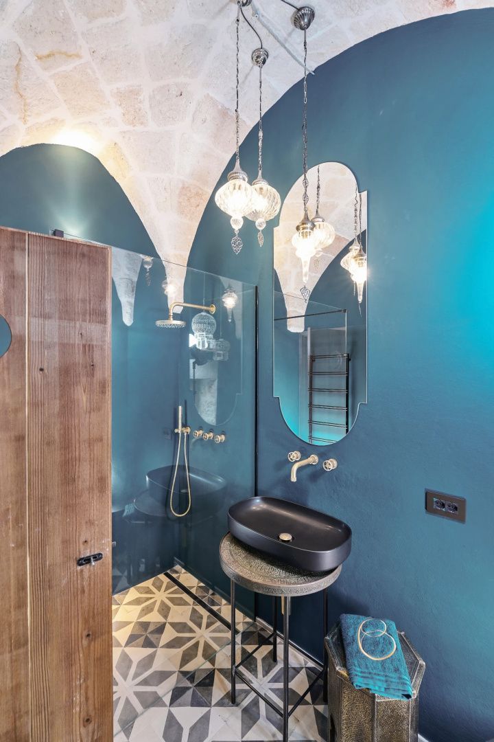 Badezimmer mit schwarzem Aufsatzwaschbecken, ovalem Spiegel, Regendusche und steinerner Gewölbedecke.