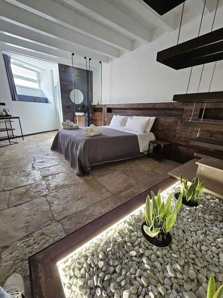 Modernes Hotelzimmer mit Steinboden, Doppelbett und kleinem Kieselbeet mit Pflanzen.