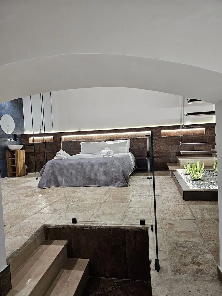 Blick durch einen Rundbogen auf ein Doppelbett mit Holzrückwand und Steinboden.