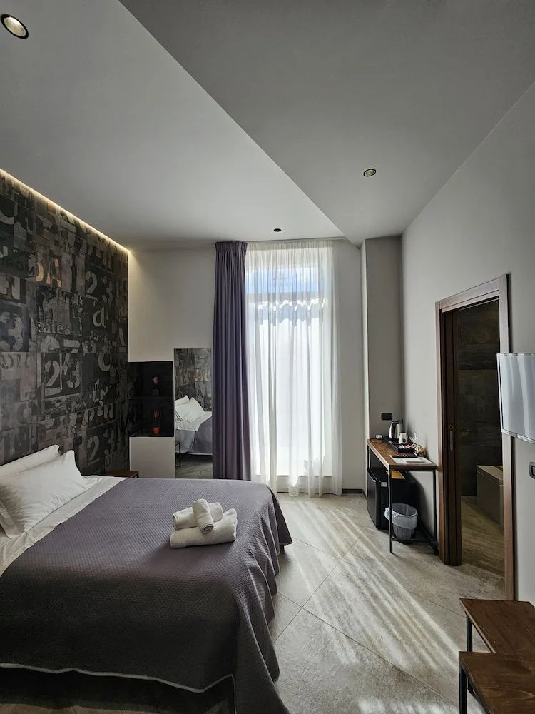 Modern eingerichtetes Hotelzimmer mit Doppelbett, dunkler Mustertapete und angrenzendem Bad.