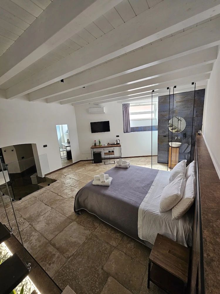 Geräumiges Zimmer mit Holzbalkendecke, Doppelbett, Steinboden und Fernseher an der Wand.