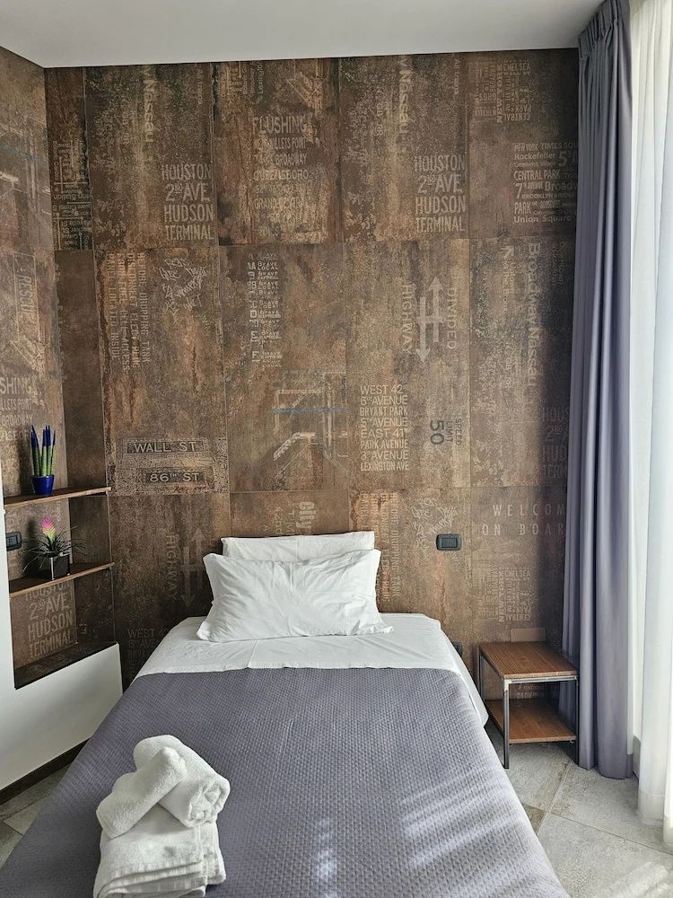 Einzelbett mit weißem Kissen vor einer braunen Wand mit Vintage Schriftdesign.