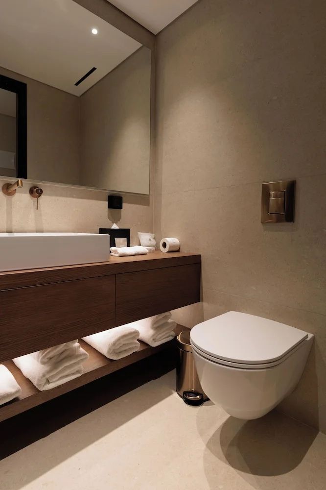 Modernes Badezimmer mit weißem Waschbecken, Holzablage und Toilette.