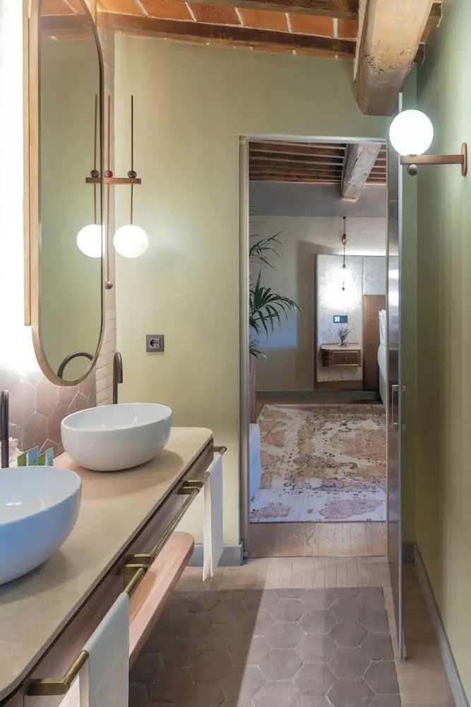 Badezimmer mit zwei Aufsatzwaschbecken, ovalem Spiegel und Blick in das angrenzende Schlafzimmer.
