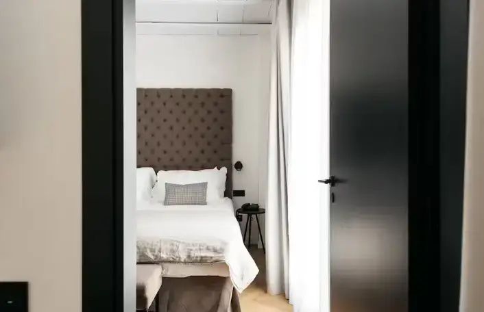Blick durch den Türausschnitt auf ein Doppelbett mit gepolstertem Kopfteil und weißer Wäsche.