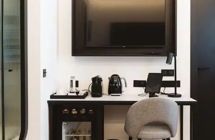 Schreibtischbereich mit Flachbildfernseher, Kaffeemaschine, Minibar und modernem Stuhl.