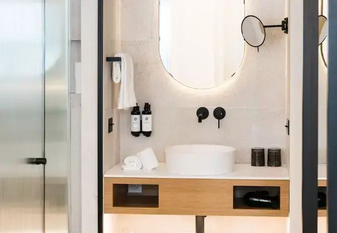 Modernes Badezimmer mit rundem Aufsatzwaschbecken, ovalem Spiegel und schwarzen Armaturen.