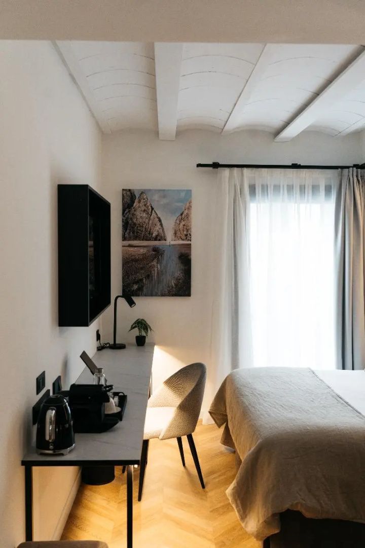 Schreibtisch mit Stuhl, Wandfernseher und Bild neben einem hellen Fenster.