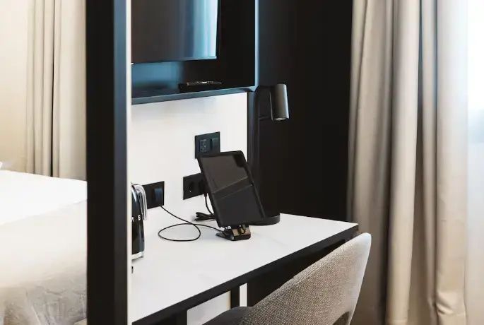 Schreibtisch im Hotelzimmer mit Tablet auf einer Ladestation, Schreibtischlampe und Stuhl.