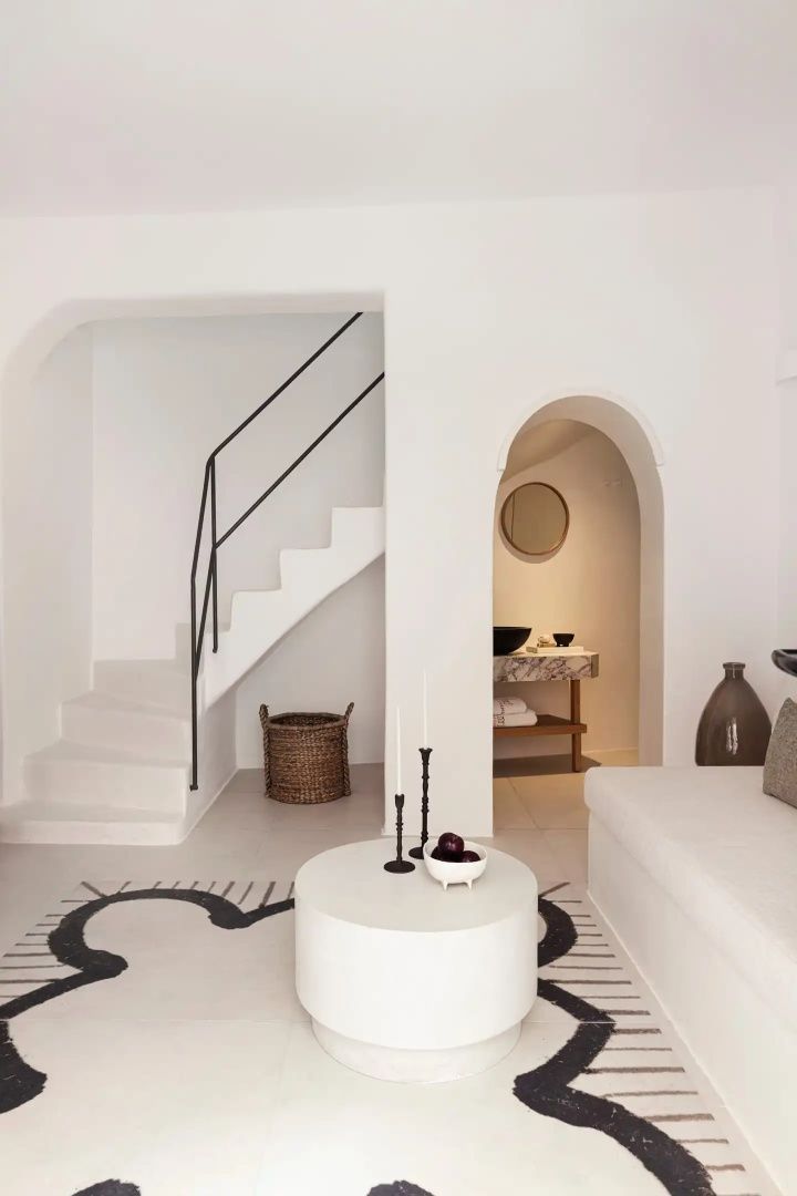 Heller Wohnbereich mit weißer Treppe, Rundbogen und minimalistischen Möbeln