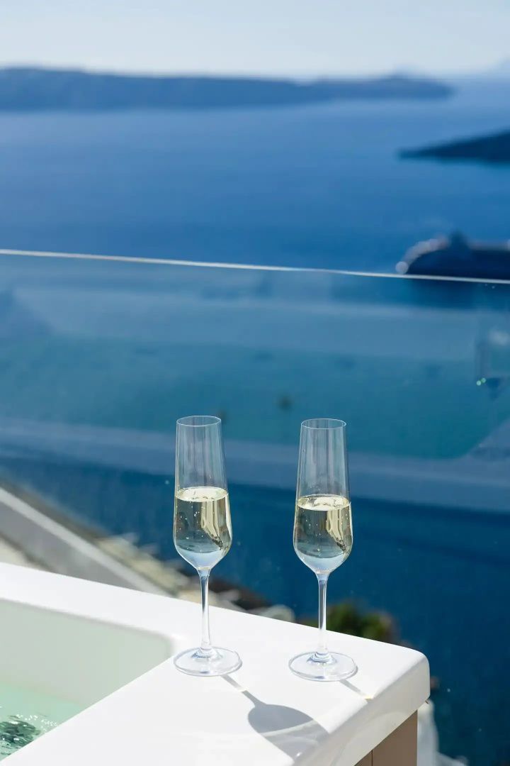 Zwei gefüllte Sektgläser auf einer Terrasse mit Glasgeländer und Blick auf das blaue Meer.