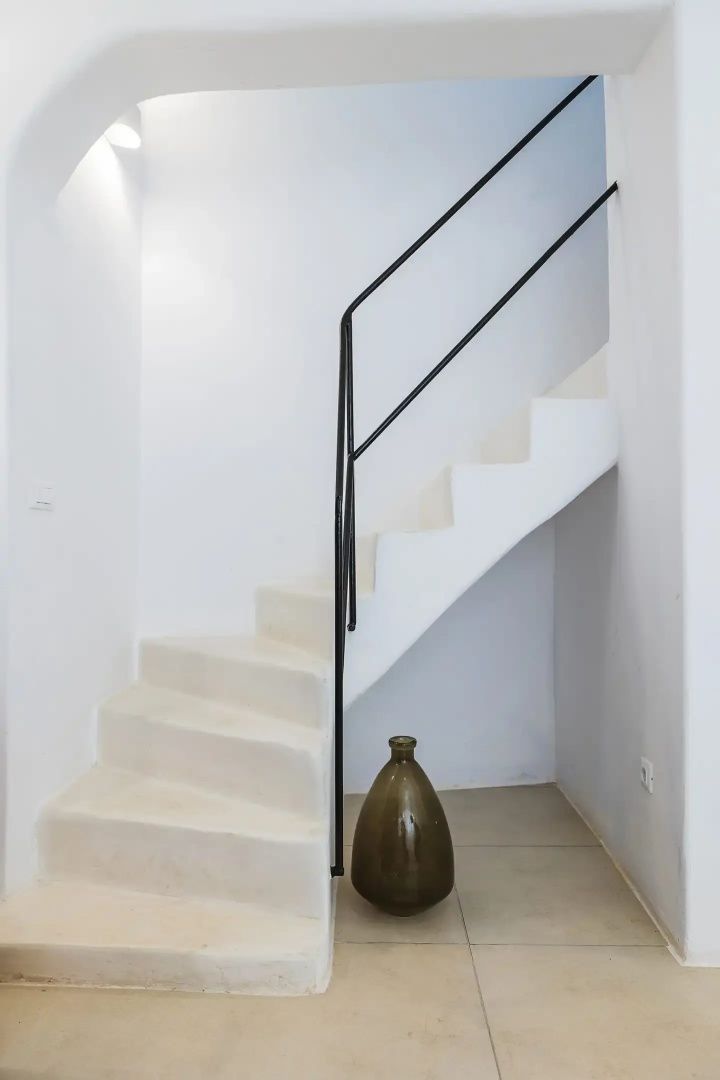 Eine geweißte Treppe mit schwarzem Metallgeländer und einer braunen Vase.