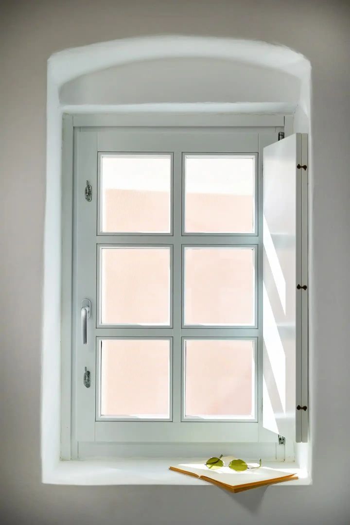 Weißes Sprossenfenster mit geöffnetem Innenladen in einer hellen Wand