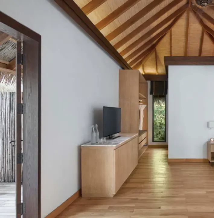 Innenbereich einer Villa mit hohem Holzgebälk, einem Sideboard inklusive Fernseher und Holzboden.