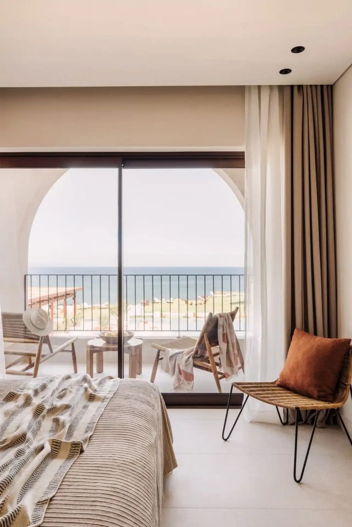 Blick vom Zimmer auf den Balkon mit Sitzmöbeln und das dahinter liegende Meer.