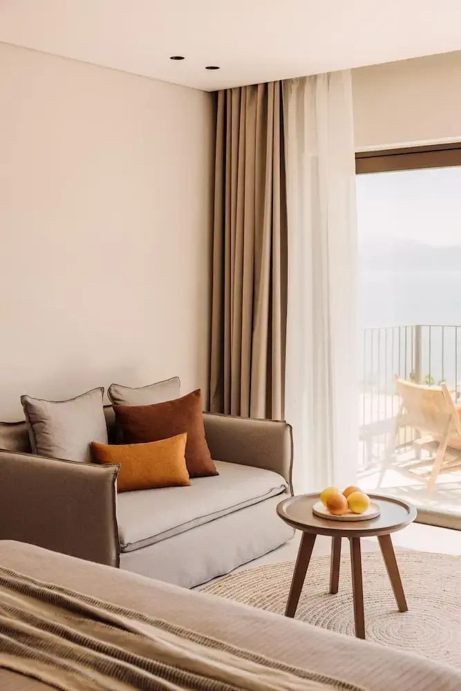 Sitzecke im Hotelzimmer mit einem grauen Sofa, bunten Kissen und Beistelltisch.
