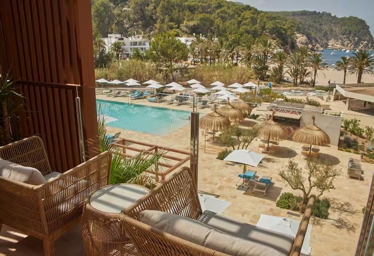 Blick von der Terrasse auf die Poolanlage, Sonnenschirme und bewaldete Hügel