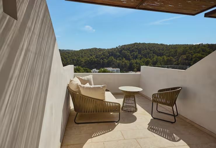 Sonnige Terrasse mit Sitzmöbeln und Blick auf bewaldete Hügel unter blauem Himmel.