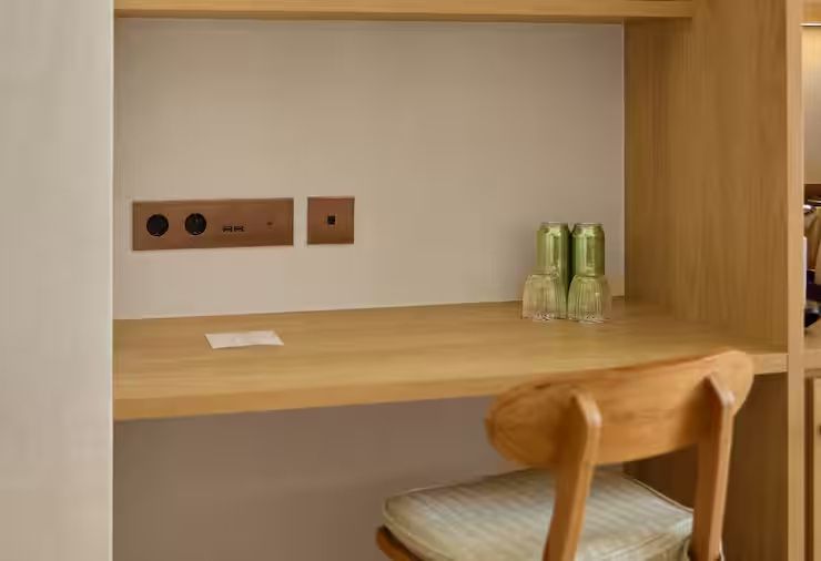 Schreibtisch aus Holz mit Holzstuhl, Steckdosen an der Wand und Gläsern.