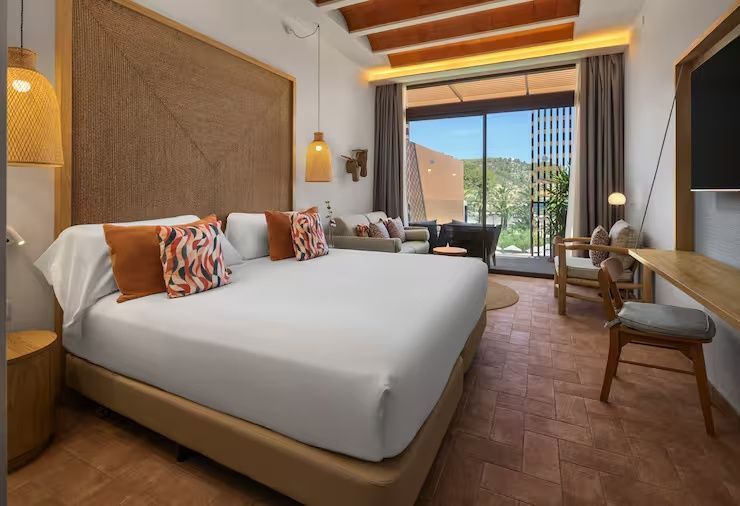 Helles Hotelzimmer mit Doppelbett, Sitzbereich und Zugang zum Balkon
