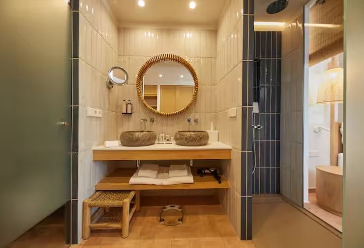 Badezimmer mit zwei Steinwaschbecken, rundem Spiegel und begehbarer Dusche
